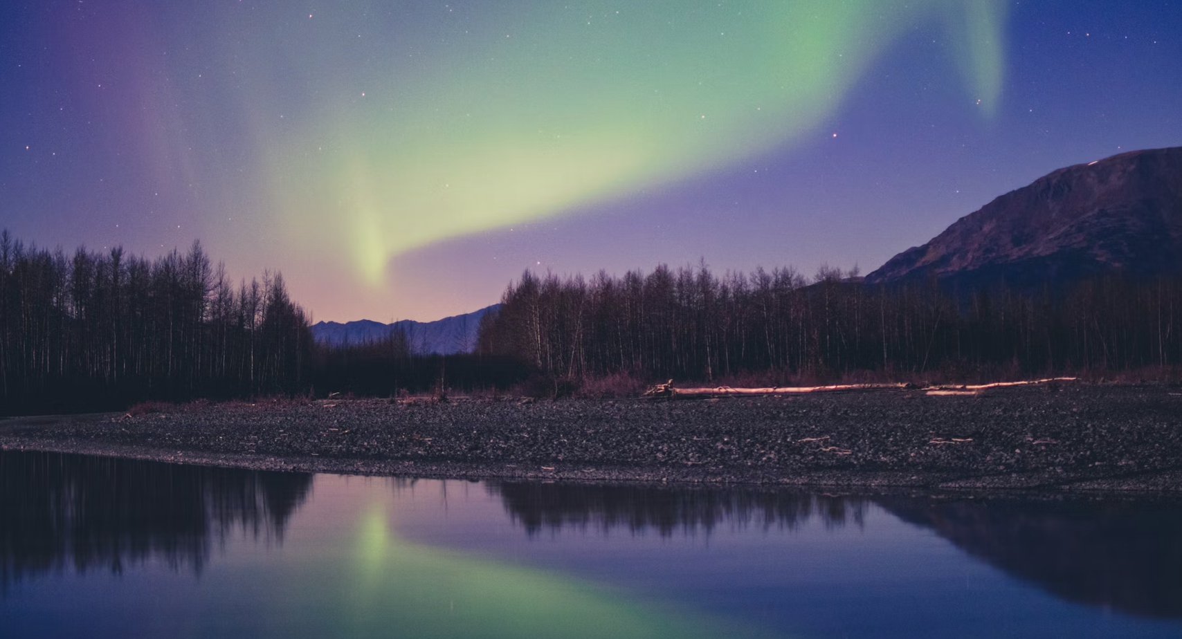 Northern Lights (Aurora Borealis) over Alaska landscape with mountains and lake reflection